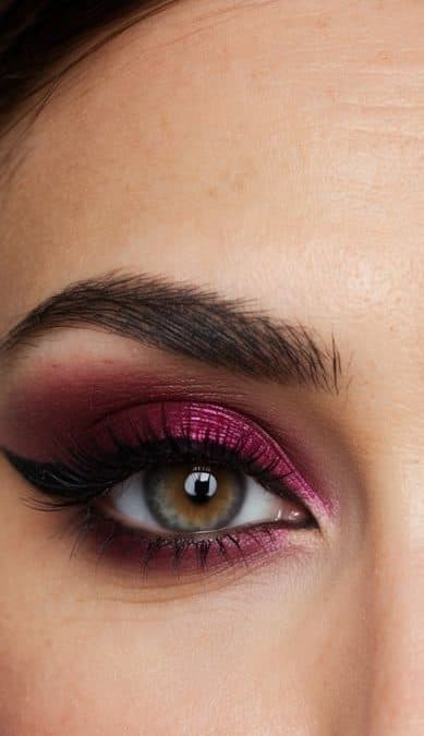 A close-up of a pair of eyes with bold and sophisticated maroon eye makeup, featuring a crimson cat eye and intricate details