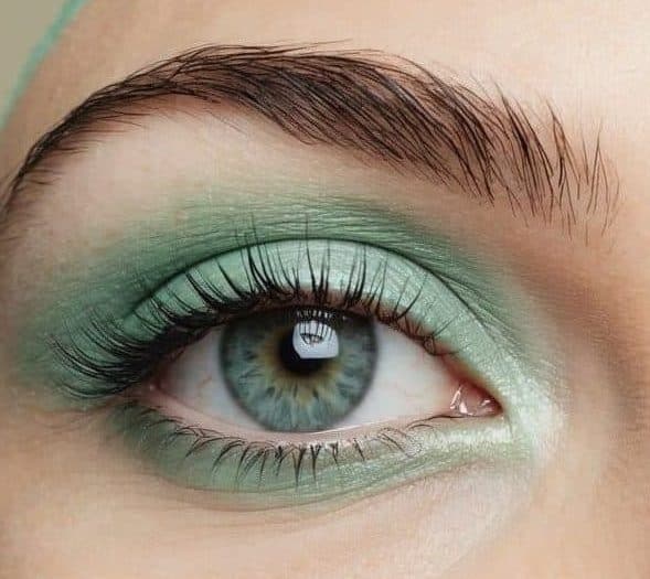 Soft pastel green eye makeup on a clean, neutral background with a hint of aqua mist