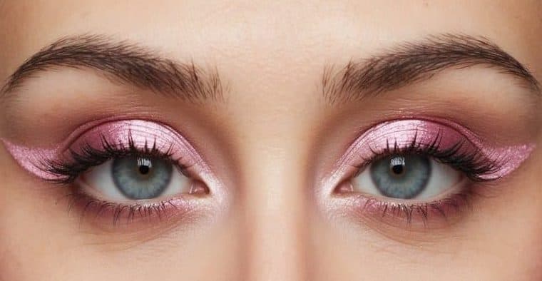 A close-up of a pair of eyes with pink metallic inner corners and pastel pink eyeliner wings