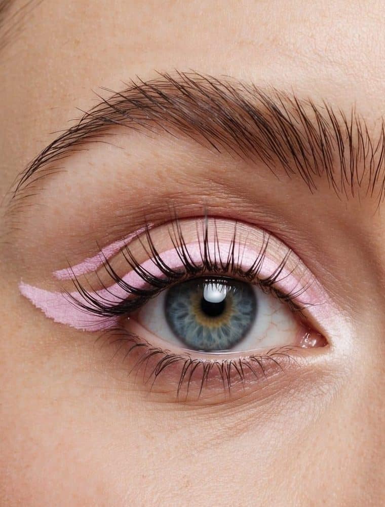 A close-up of an eye with a delicate swirl of pink eyeliner, accented with a pastel wing at the outer corner