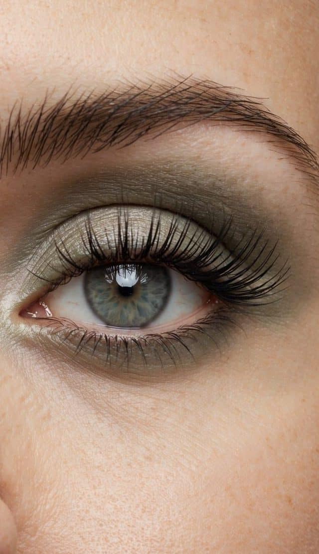 A close-up of a serene eye with soft, smoky sage eyeshadow, framed by long, wispy lashes and a subtle shimmer on the lid