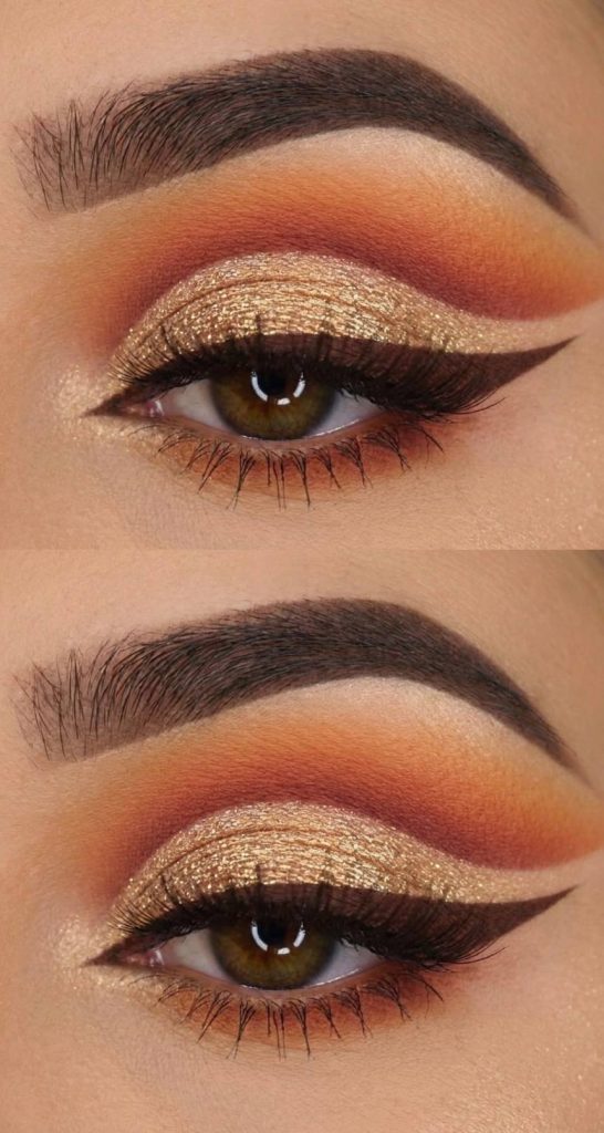 Close-up of an eye with bold makeup featuring sparkly gold glitter on the eyelid, dark eyeliner with a winged tip, and blended orange and brown eyeshadow in the crease and above, with well-defined eyebrows.