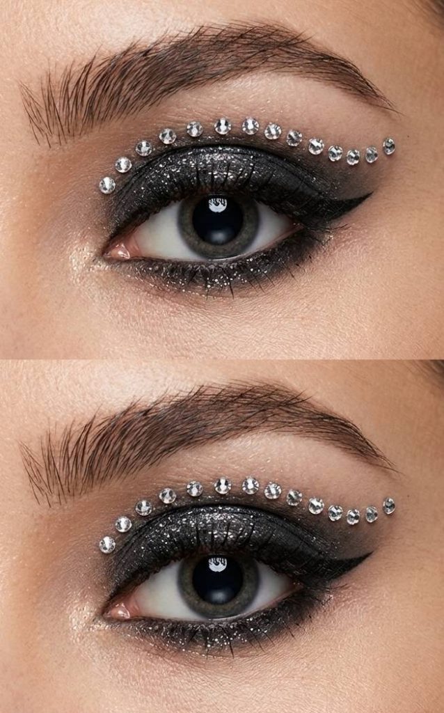 Sharp black eyeliner and glitter lid with arched rhinestone line above the crease in a sleek rhinestone eye makeup idea.