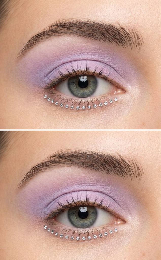 A rhinestone eye makeup idea featuring soft lilac shadow and floating crystals beneath the eye, resembling a breeze-blown shimmer.