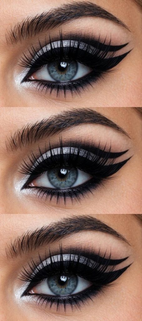Trad goth eye makeup look with twin graphic eyeliner wings, bold white shimmer in the inner corner, and full fluttery lashes.